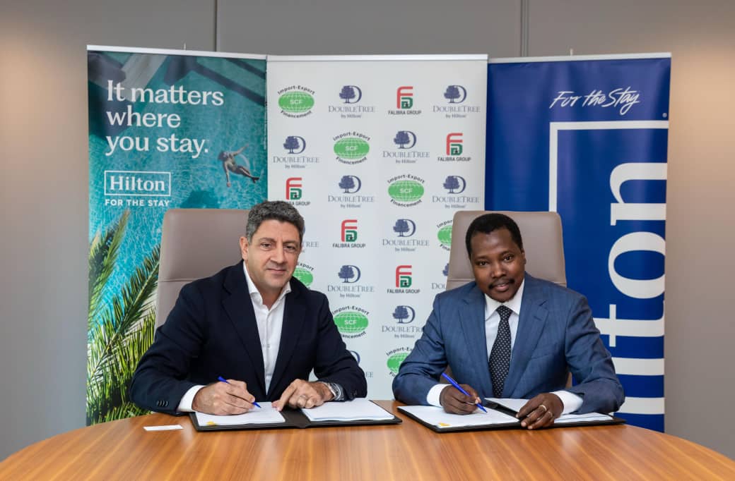 Deux représentants signent l’accord du projet DoubleTree by Hilton Conakry Kaloum devant les logos des partenaires